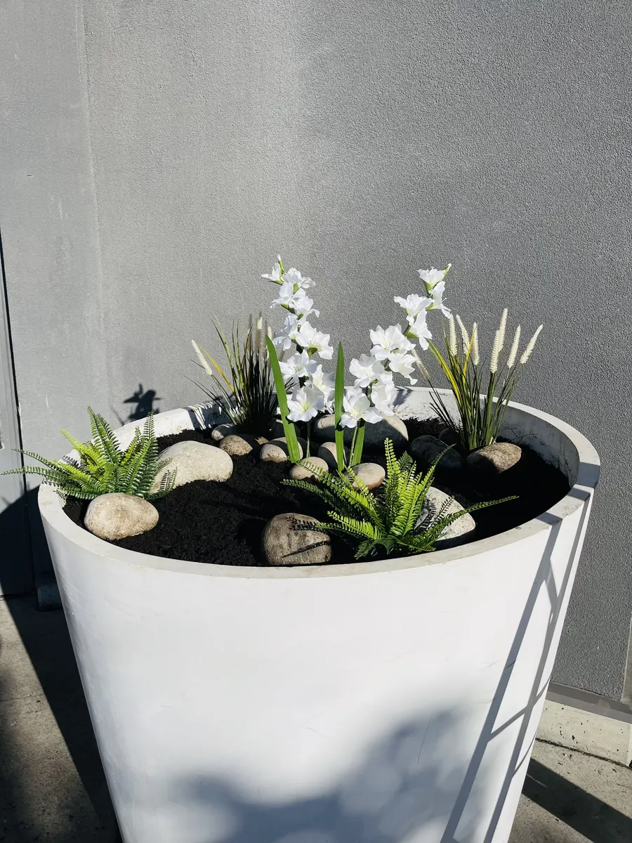 Custom white planter with flowers, ferns, and river stones